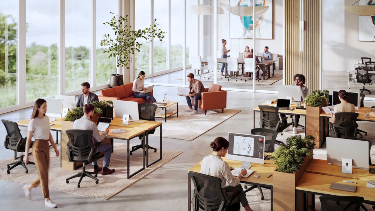 A bright, modern open-plan office with multiple people working at desks, seated in chairs, and using computers. Large floor-to-ceiling windows let in natural light, and the space includes wood flooring, beige rugs, plants, and a few accent seating areas.